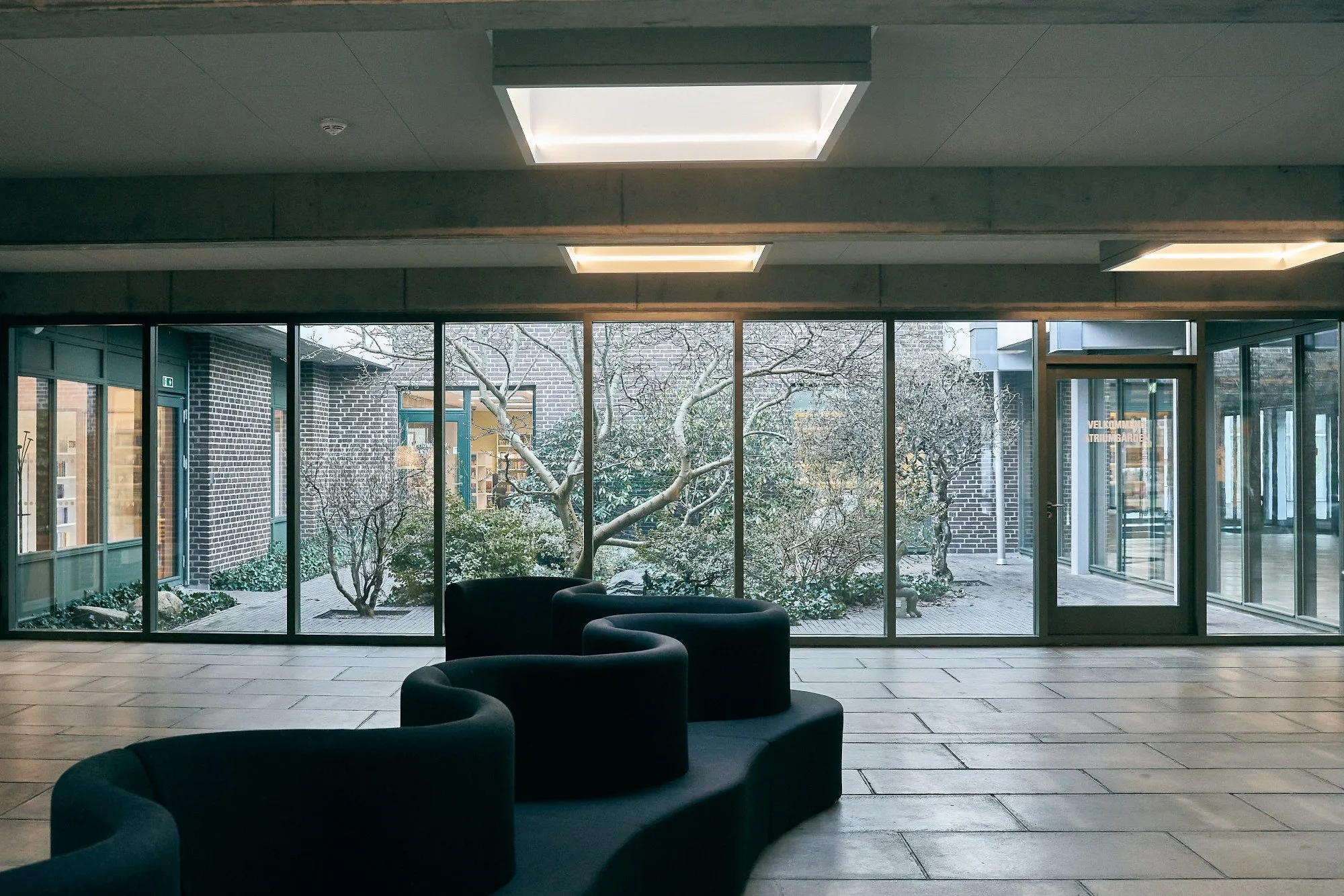 Billund Centret efter renoveringen: lys forhal med mørke, bølgede sofaer og glasvæg ud mod en have