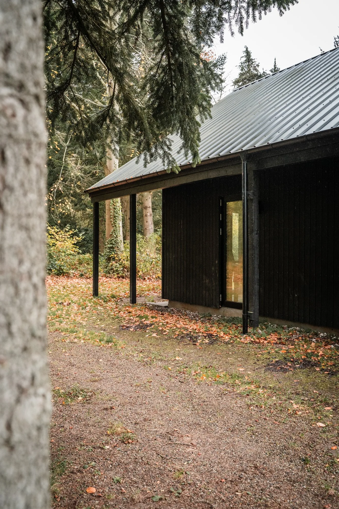 Spejderhyttens hjørne i sort træ med overdækket gang under taget