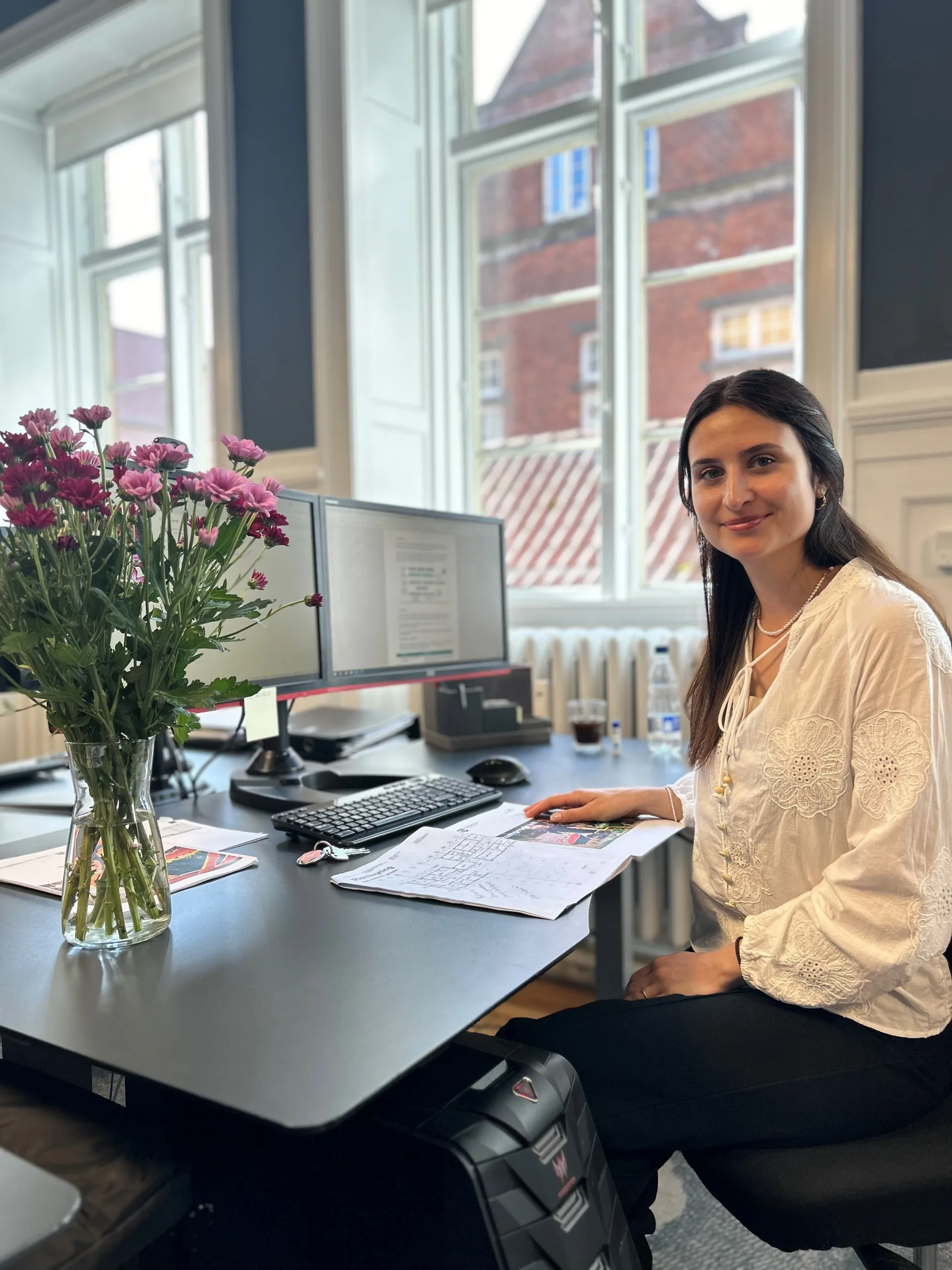 Marina Hedegaard ved sit skrivebord på tegnestuen med blomster i vinduet